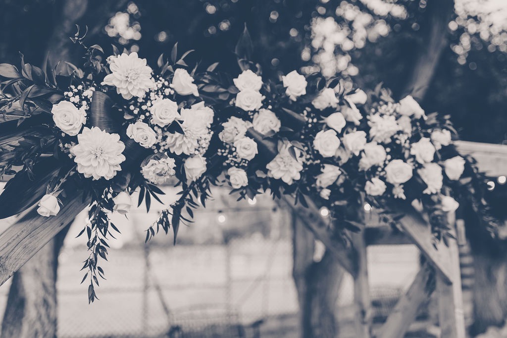 Flowers on Rustic Wood Wedding Arch B&W | 5 Different Types of Wedding Venues to Consider | Mill Pond Farms | Choosing Between Wedding Venue Type: Barn & Historic Home