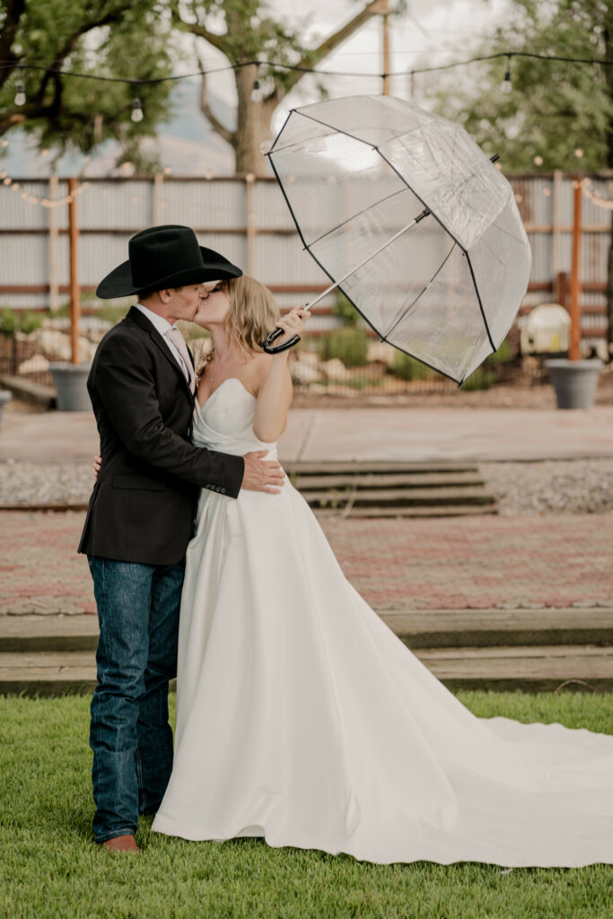 Bride & Groom Kissing Under Clear Umbrella | Backup Plans for Your Outdoor Wedding | Millpond Farms Event Center | Rain Plan for Outdoor Wedding Venues | Utah